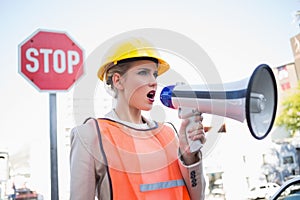 Businesswoman wearing builders clothes shouting in megaphone