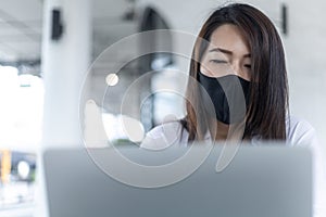 Businesswoman wearing facial mask reading bad news on line in a laptop during coronavirus outbreak. impact of COVID-19