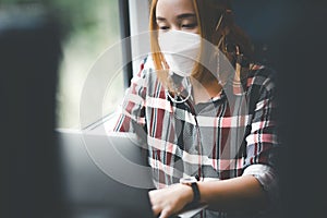 Businesswoman wearing a mask and working on laptop on a train, Asian freelance writer or designer writing emails on computer, work