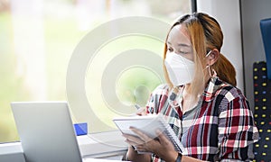 Businesswoman wearing a mask and working on laptop on a train, Asian freelance writer or designer writing emails on computer, work