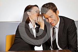 Businesswoman whispering in businessman's ear at office