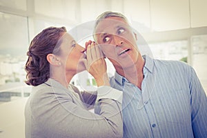 Businesswoman whispering gossip to her colleague