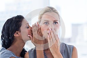 Businesswoman whispering gossip to her colleague