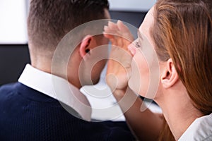 Businesswoman Whispering Into Male Partner`s Ear
