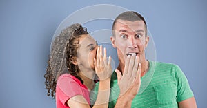 Businesswoman whispering in shocked colleague`s ear against blue background