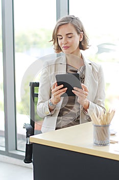 Businesswoman in white suit hand holding tablet for searching on website and thinking in job at workspace in office