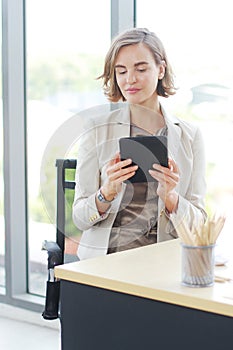 Businesswoman in white suit hand holding tablet for searching on website and thinking in job at workspace in office