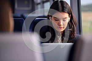 Businesswoman With Wireless Earbuds Commuting To Work On Train Working On Laptop