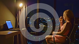 Businesswoman work on laptop in room hotel.Desk lamp, large window, night city.Freelancer work on computer in house high