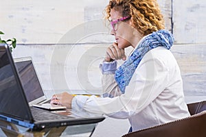 Businesswoman at work in a workplace indoor home place - woman working with two personal laptop computer - concept of office and photo