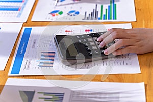 Businesswoman working on calculator to calculate business data financial report on wooden table.