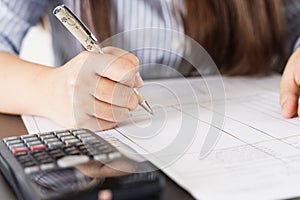 Businesswoman working on desk office holding pen and using a calculator to calculate the numbers. Expenses, taxes, home budget