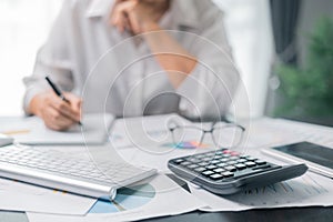 Businesswoman working on desk office with using a calculator to calculate the numbers, finance accounting concept. Woman