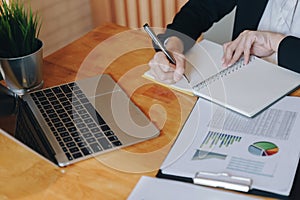 Businesswoman working with financial data and writing make note in opened notebook on wooden table. Business financial and