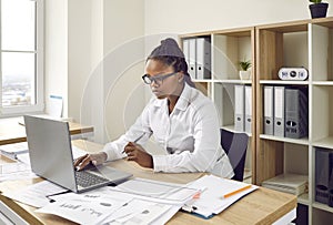 Businesswoman working in her office, using a laptop computer, and doing paperwork