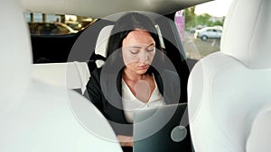 Businesswoman working with laptop and checking time on the smartwatch while traveling on the back seat in the car