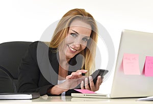 Businesswoman working at laptop computer office desk sending text message on mobile phone