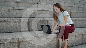 Businesswoman working on laptop outside. Executive typing on laptop at street