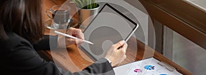 Businesswoman working on mock-up tablet with stylus pen and paperwork on wooden counter bar