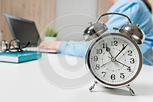 Businesswoman working in the office, in focus, an alarm clock on