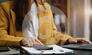 Businesswoman working with smartphone and using a calculator to calculate the numbers of static in office. Finance accounting