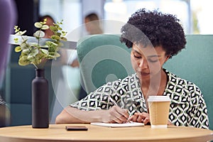 Businesswoman Working At Table In Breakout Seating Area Of Office Building Talking On Mobile Phone