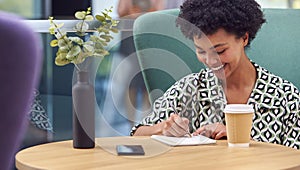 Businesswoman Working At Table In Breakout Seating Area Of Office Building Talking On Mobile Phone