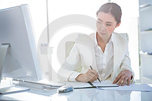 Businesswoman writing on diary on desk