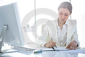 Businesswoman writing on diary on desk