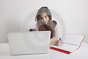Businesswoman writing in diary while looking at laptop in office