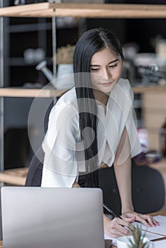 Businesswoman writing while looking at laptop screen