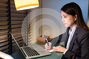 Businesswoman writing on the note with laptop computer