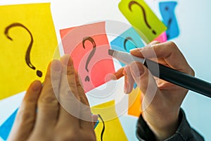 Businesswoman writing question marks on colorful sticky note paper