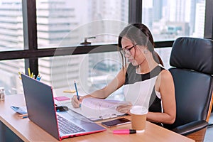 Businesswoman writing report sitting on desk with laptop and documents in office. Women working pressing calculator