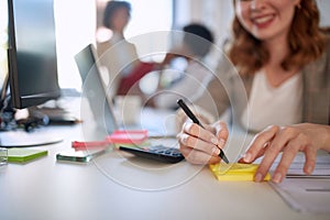 Businesswoman writing on a stickynote. Smiling woman taking notes at work