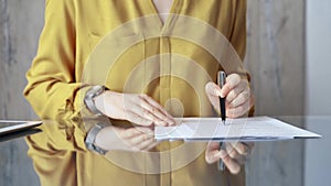 Businesswoman in yellow blues analyzing document at desk. Close-up of a professional auditor or lawyer reviewing a