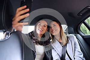 Businesswomen Commuting To Work In Back Of Car Or Taxi Taking Selfie On Mobile Phone