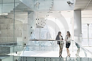 Businesswomen conversing against railing in office