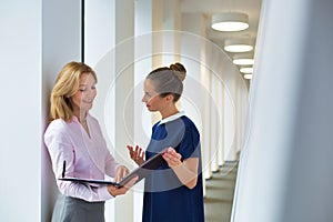 Businesswomen discussing over document while standing in corridor at office