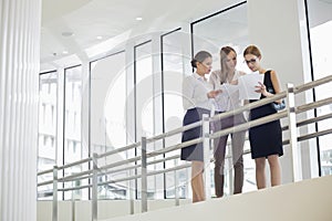 Businesswomen discussing over paperwork against railing