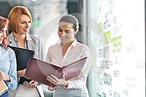 Businesswomen with file folders discussing in office corridor