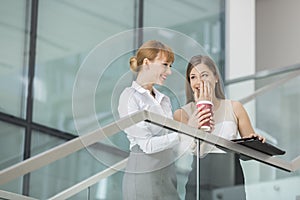 Businesswomen gossiping while having coffee on steps in office