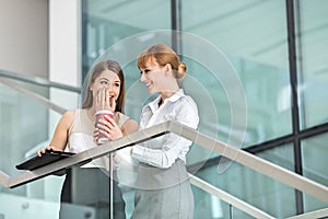 Businesswomen gossiping while having coffee on steps in office