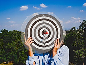 Businesswomen hand holding dart Board on blue sky and city view background, Setting challenging business goals And ready to