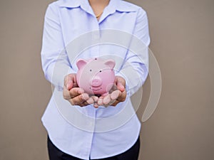 Businesswomen hand holding pink piggy bank on brown cement wall background, Saving money for future plan and retirement fund