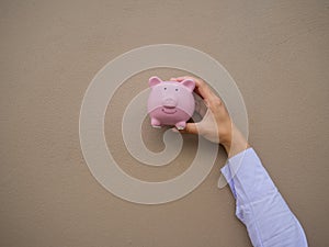 Businesswomen hand holding pink piggy bank on brown cement wall background, Saving money for future plan and retirement fund