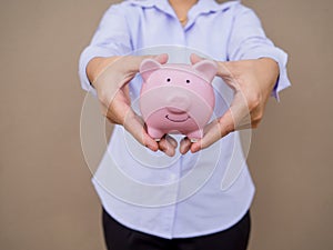 Businesswomen hand holding pink piggy bank on brown cement wall background, Saving money for future plan and retirement fund