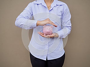 Businesswomen hand prevent pink piggy bank on brown cement wall background, Saving money for future plan and retirement fund