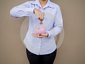 Businesswomen hand putting gold coin into pink piggy bank on brown cement wall background, Saving money for future plan