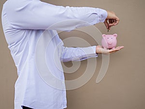 Businesswomen hand putting gold coin into pink piggy bank on brown cement wall background, Saving money for future plan